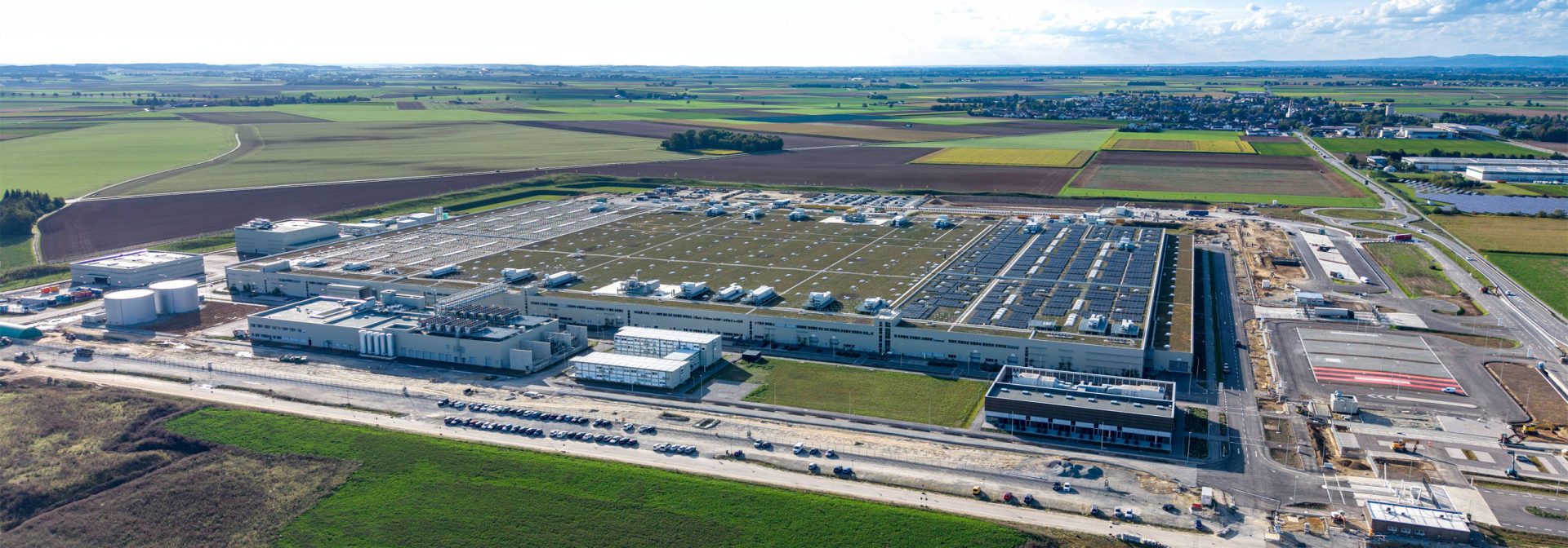 Aerial view of a large industrial facility with multiple buildings, tanks, and parking areas in a rural setting.