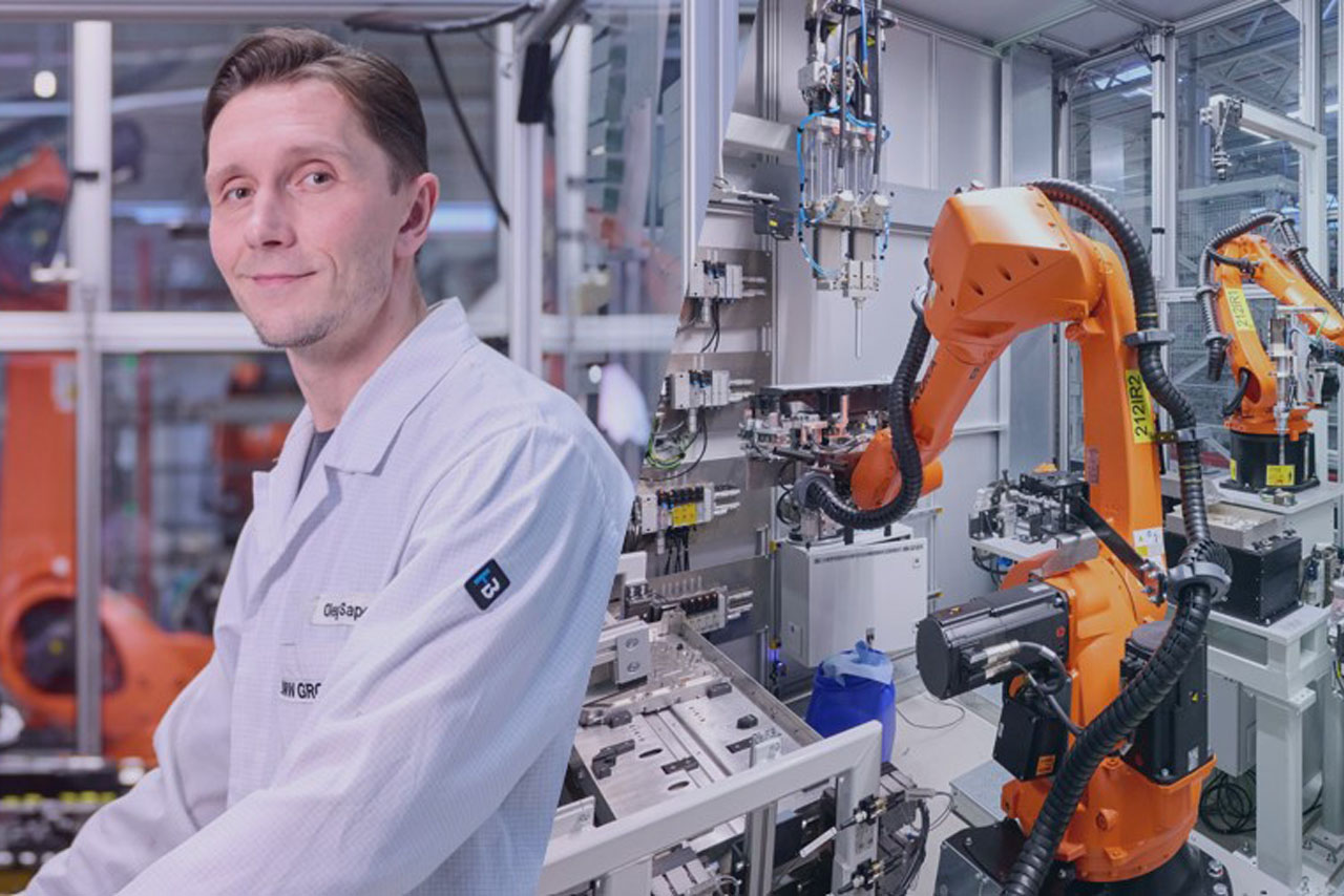 Ein Wissenschaftler in einem Laborkittel posiert neben einem Roboter und lächelt in die Kamera.