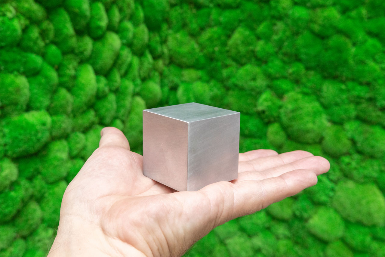 Eine Hand zeigt einen Metallwürfel vor einem Hintergrund aus grünem Moos.