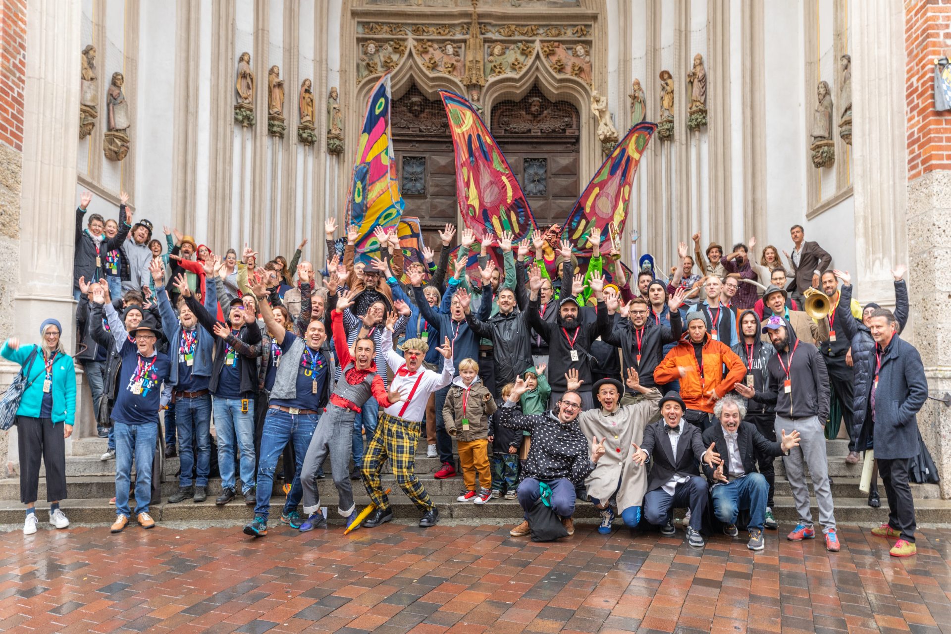 A large group of people pose with flags in front of a historic building.