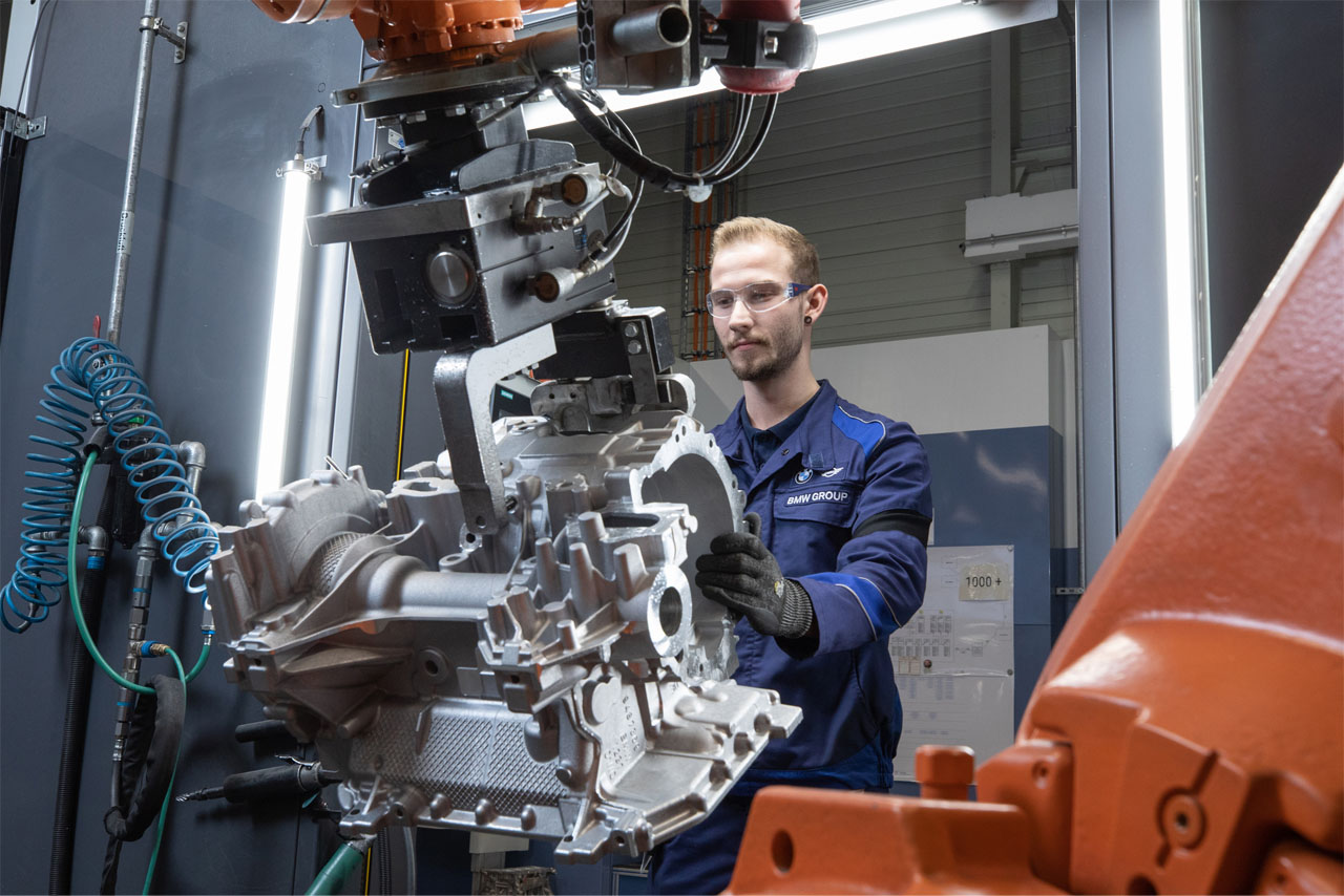 An employee working on a component with a modern robot in the light metal foundry.