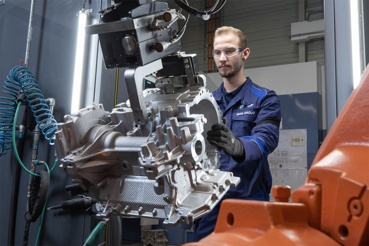 A man in a blue shirt operates a machine, focused on his task in a workshop environment.