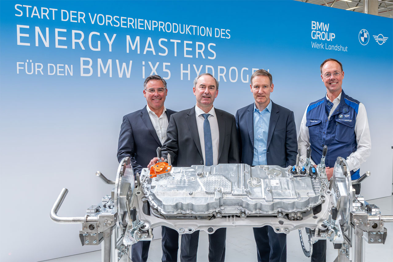 Four men in suits and workwear stand behind a large technical component in front of a wall with the text 'Start of pre-series production of the Energy Master for the BMW iX5 Hydrogen'.