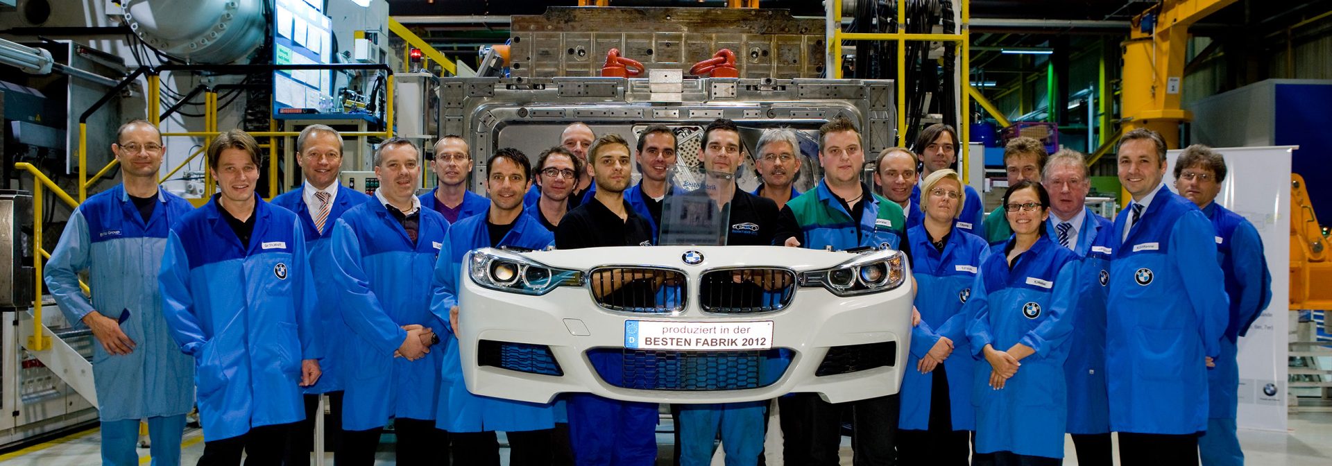People show the camera a finished front of a BMW with the inscription “Best Factory 2012”