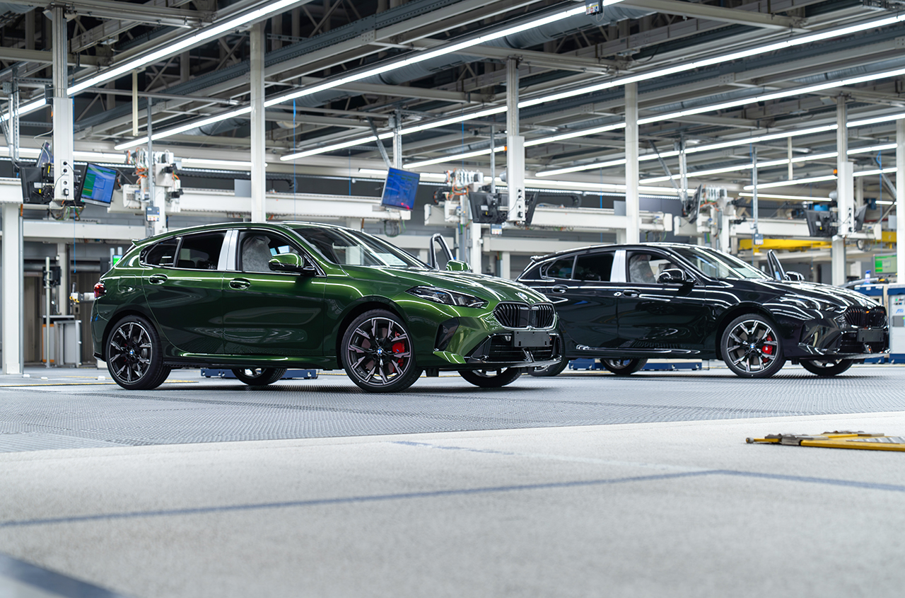 Grünes BMW Modell neben einem schwarzen in einer Fabrikhalle.