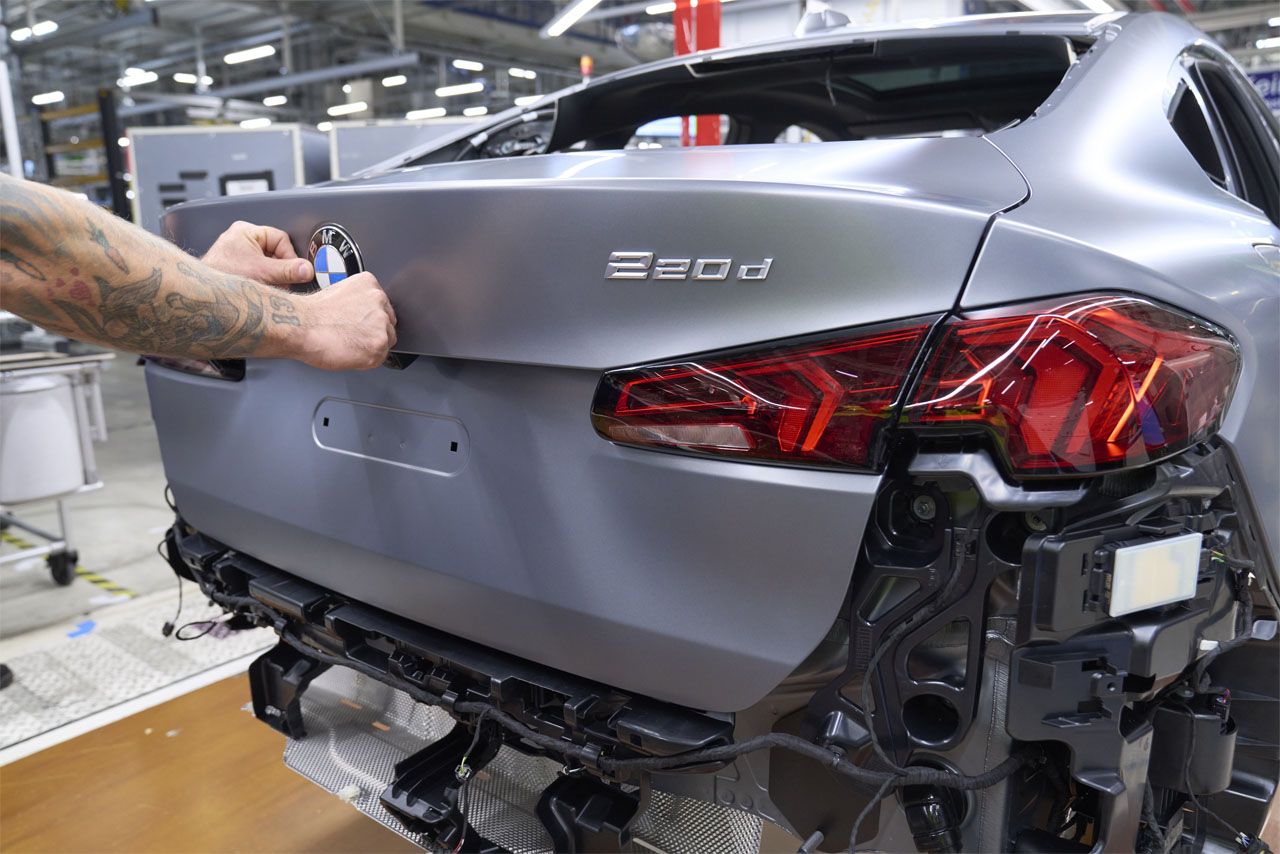 In einer Fabrik repariert ein Mann ein Auto. Um ihn herum sind verschiedene Werkzeuge und Ausrüstungen.