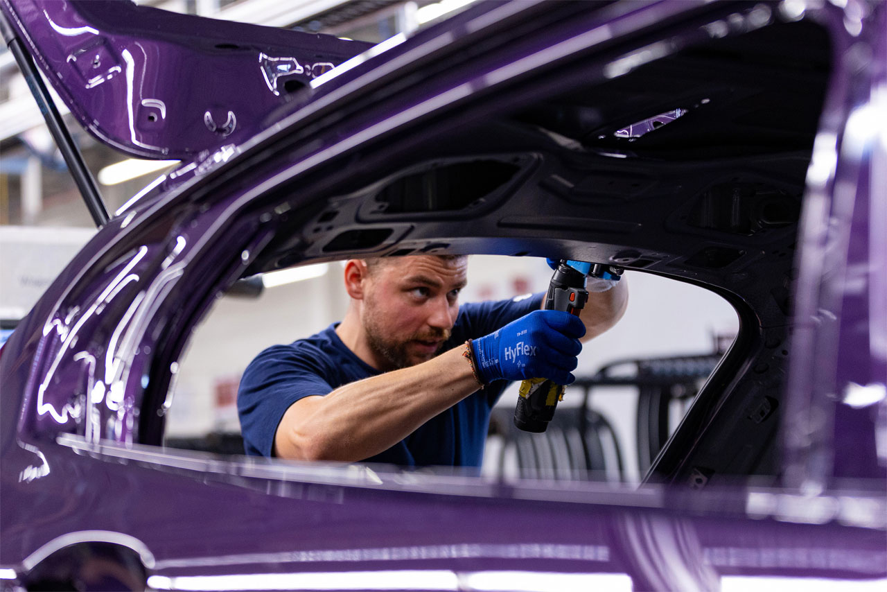 Ein Mann führt Arbeiten an einem lila Auto in einer Produktionsstätte durch.