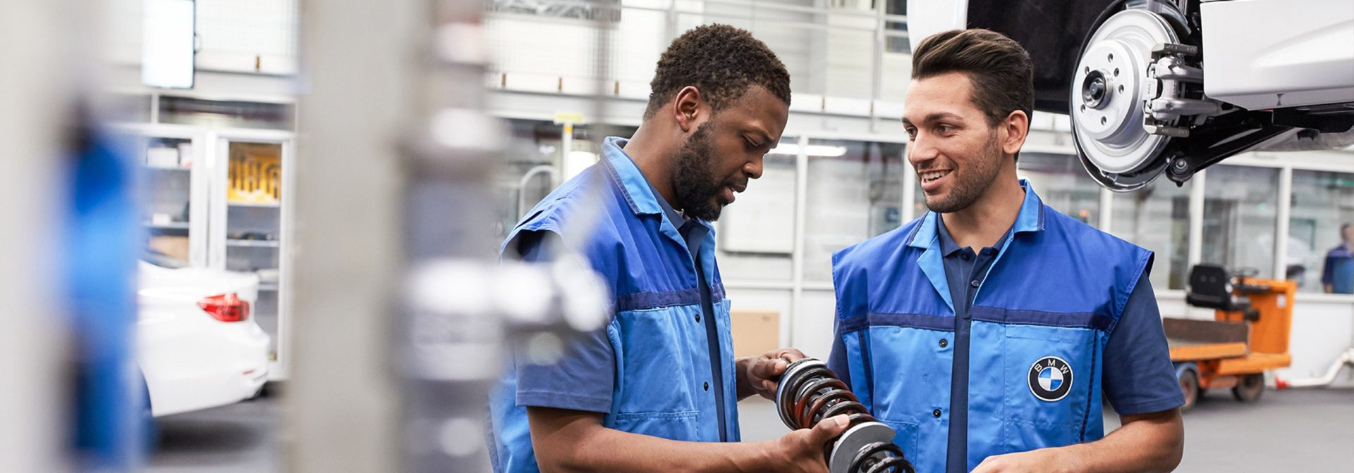 Zwei Mechaniker arbeiten an einem BMW-Teil in einer Werkstatt.