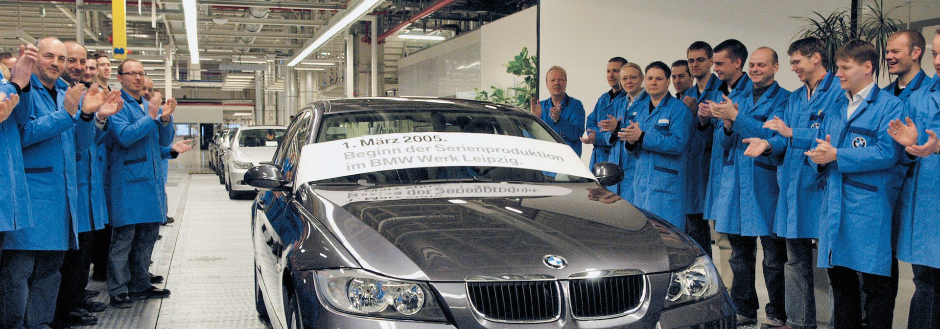 Mehrere Männer versammeln sich um einen BMW 3er aus dem Jahr 2005 und applaudieren.
