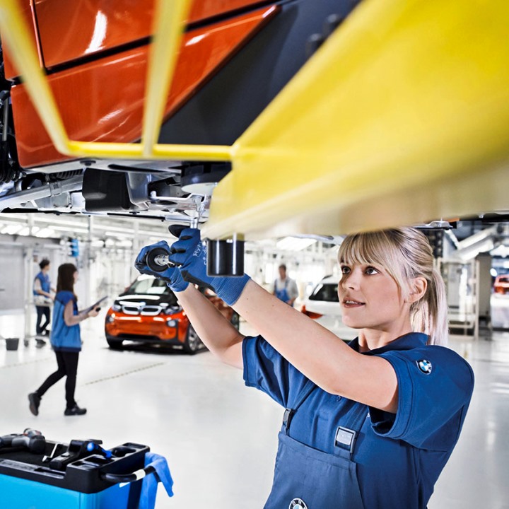 A young woman works on the underbody of a vehicle.
