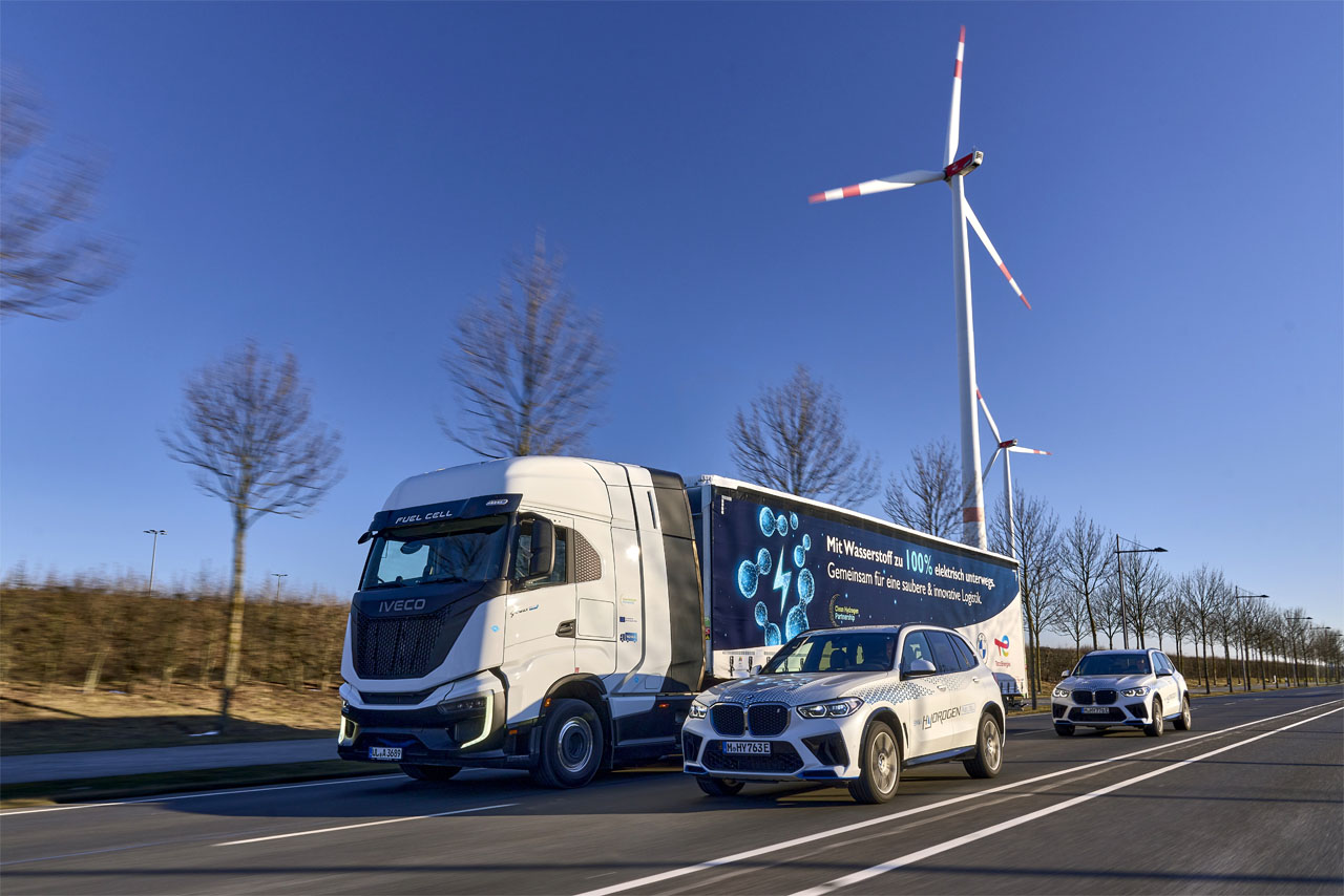 A hydrogen truck and two BMW hydrogen cars drive along a road.