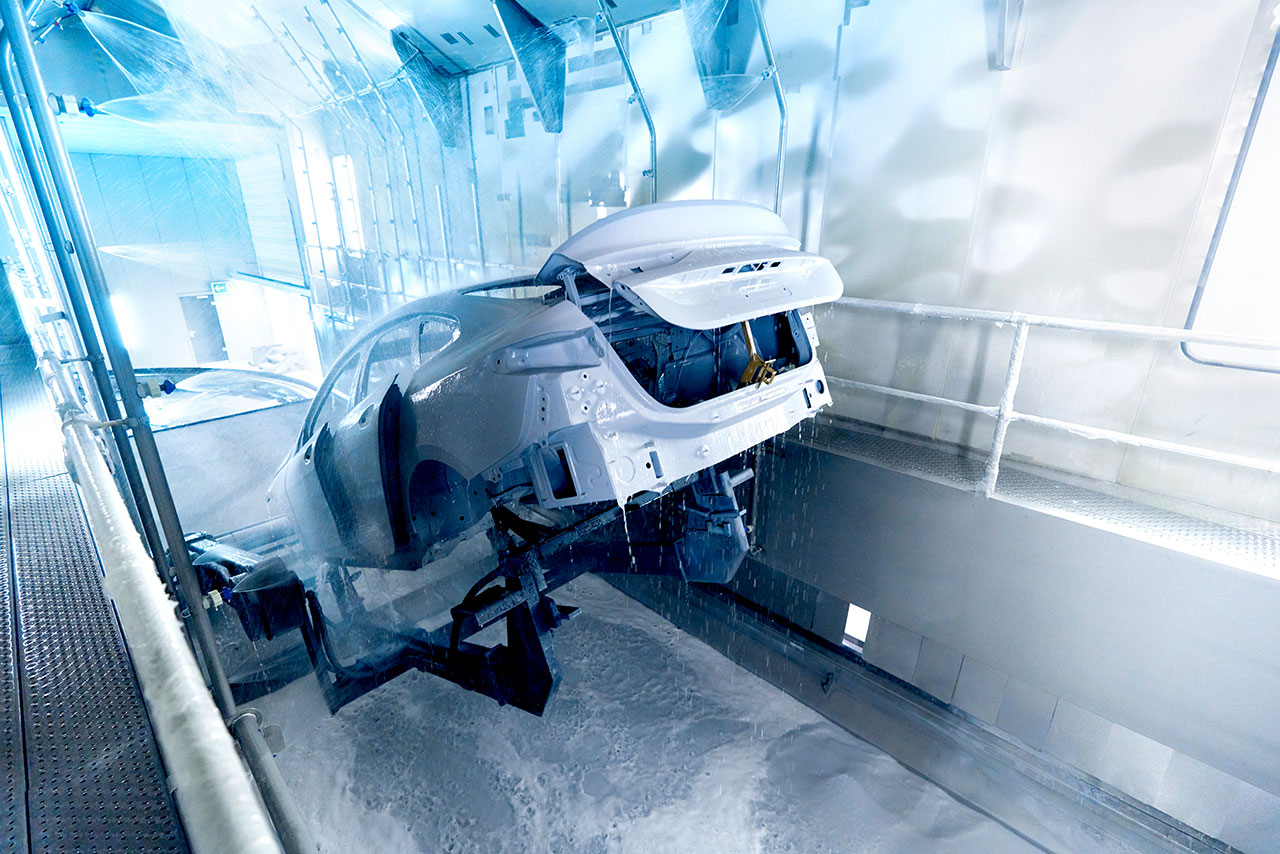 Vehicle body in the paint shop being dipped into a dip tank by a machine for cleaning.