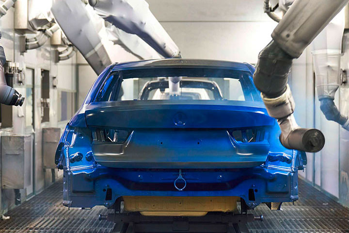 Roboterarme, welche die Karosserie eines BMW Fahrzeuges blau lackieren.