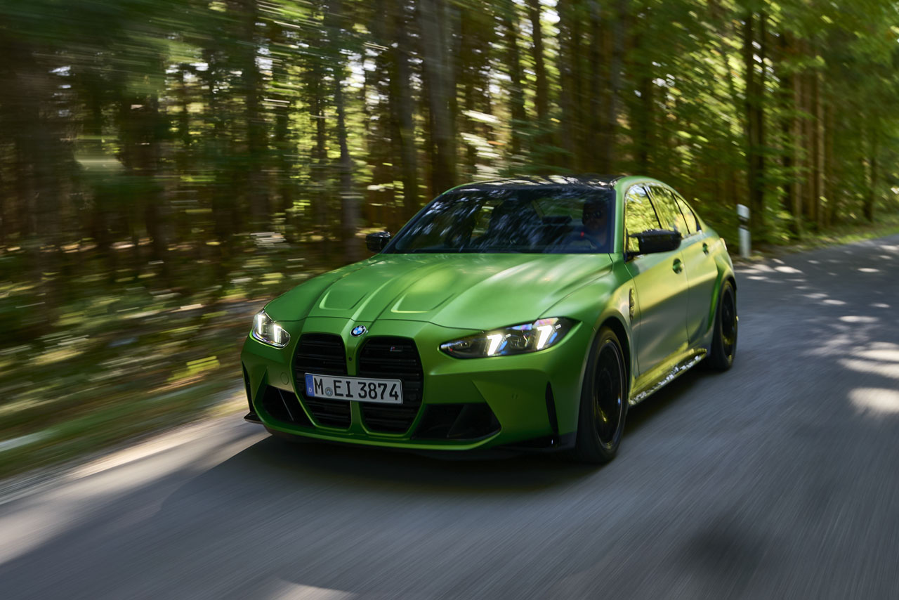 Grüner BMW M3 auf einer Straße, die durch einen Wald führt.
