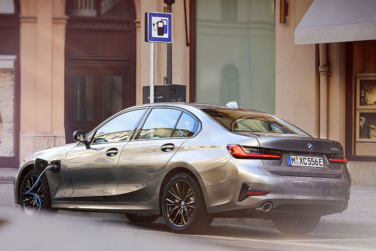 Grauer BMW 3er Plug-In-Hybrid steht angesteckt auf einem Parkplatz für Elektroautos in einer Stadt.
