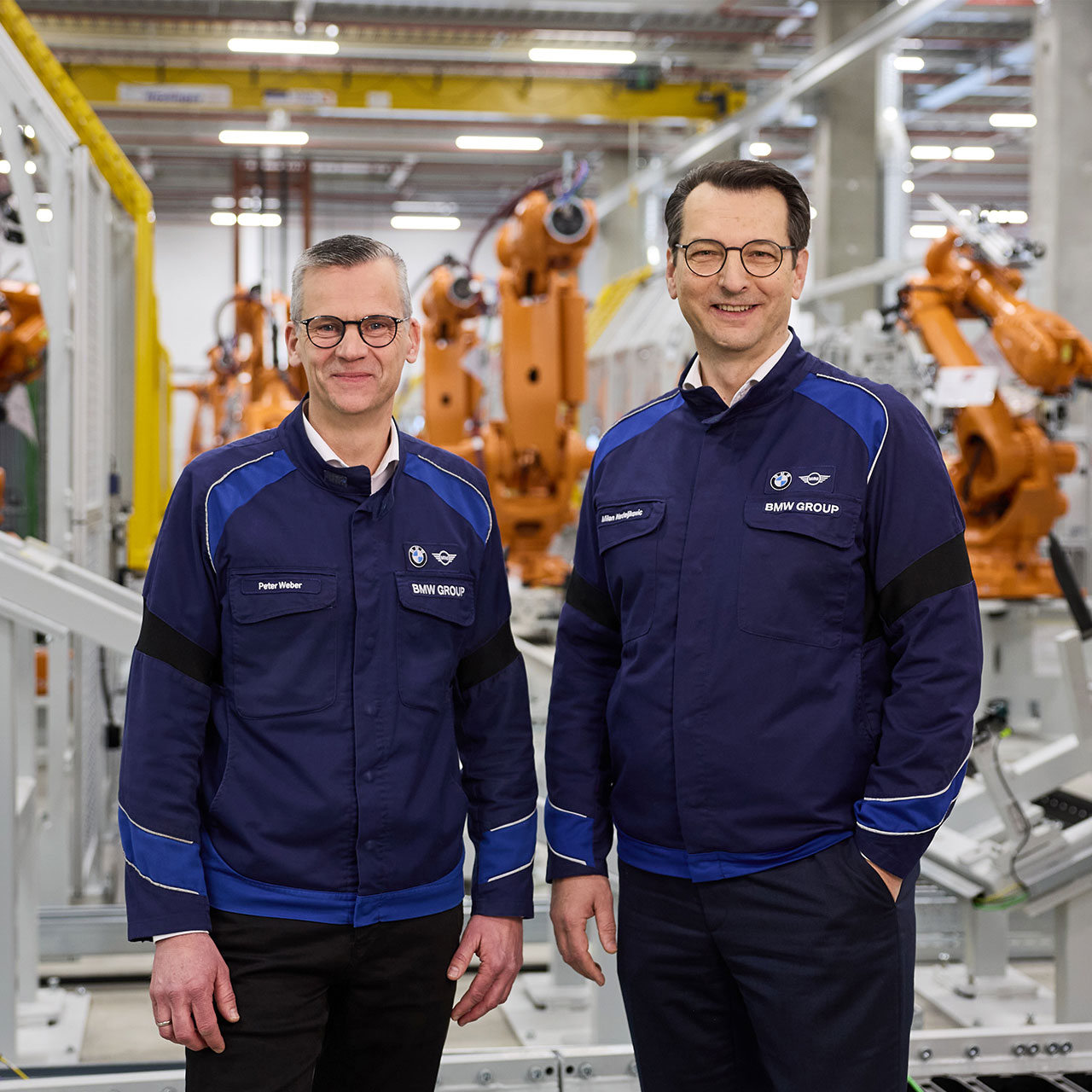 Zwei Mitarbeiter der BMW Group stehen zwischen Produktionsrobotern.