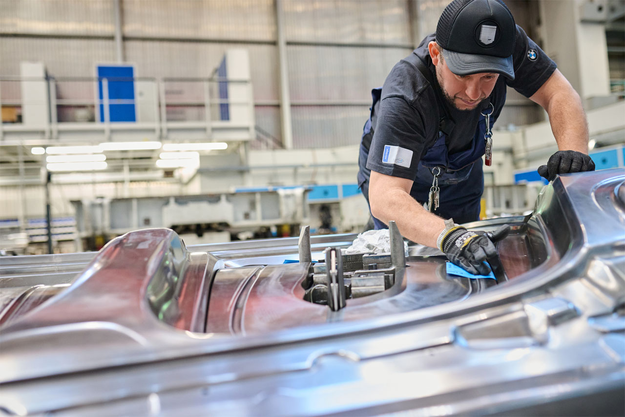 A man in work clothes and gloves is polishing a large metal mold in a factory.