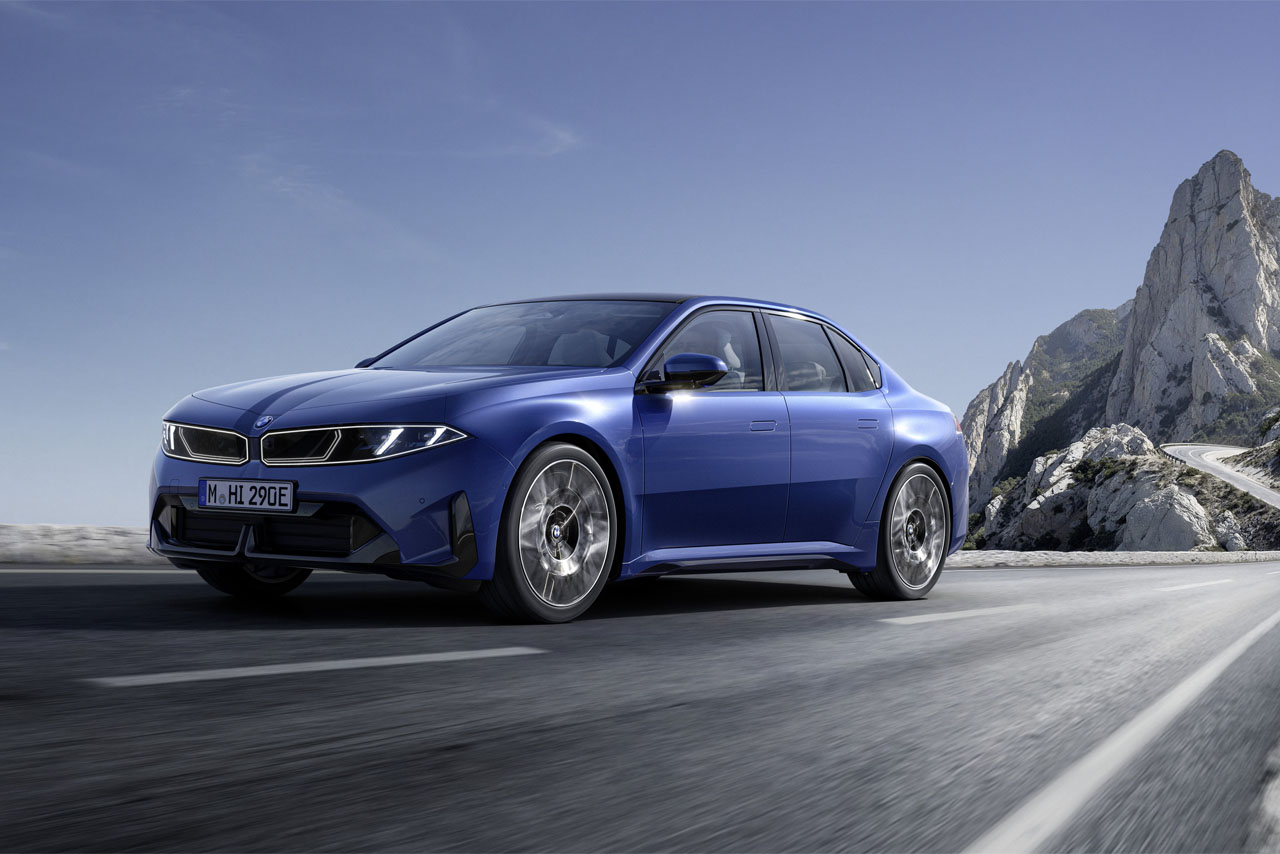 A blue BMW i3 driving on a mountain road with rocks in the background
