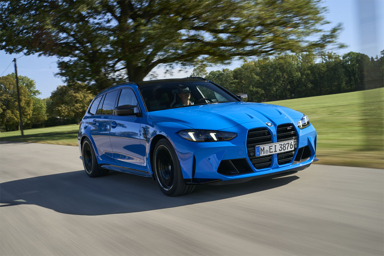 Blue BMW M3 Touring driving on a country roads next to a huge open field.