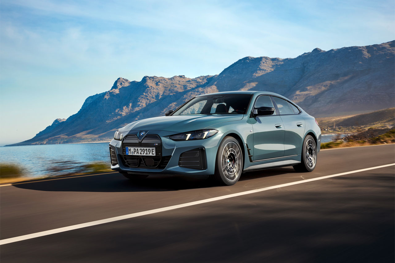 Grey BMW i4 driving on a country road along the ocean with mountains in the background.