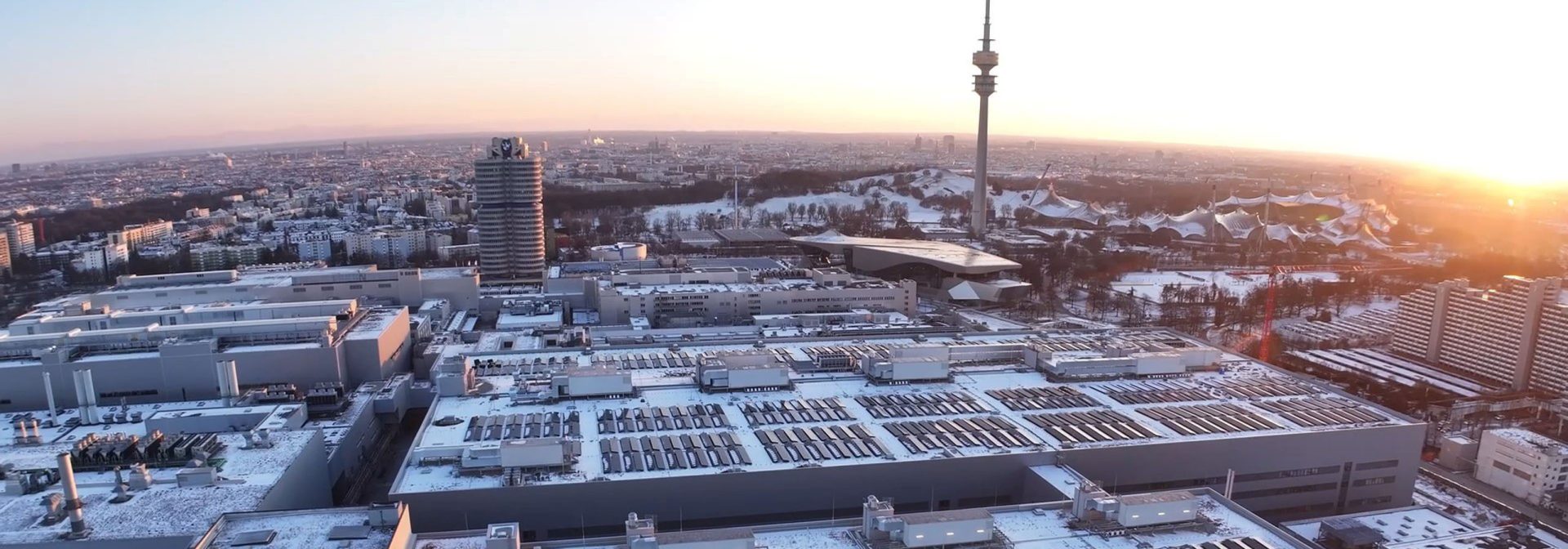 Aerial view of the BMW plant in Munich with the Olympic Tower in the background at sunset.