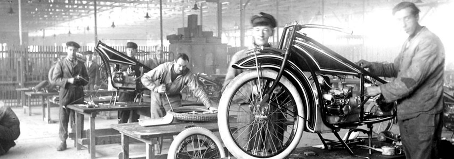 Early 20th-century motorcycle assembly line with workers.