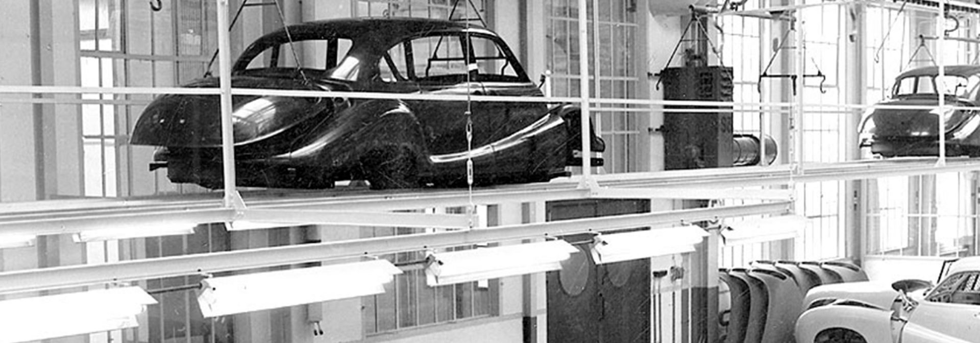 Black and white image of cars on an assembly line in a factory.