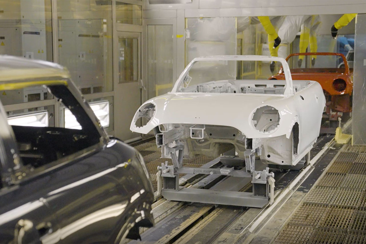  A mechanic works on a car inside a factory, surrounded by tools and equipment.