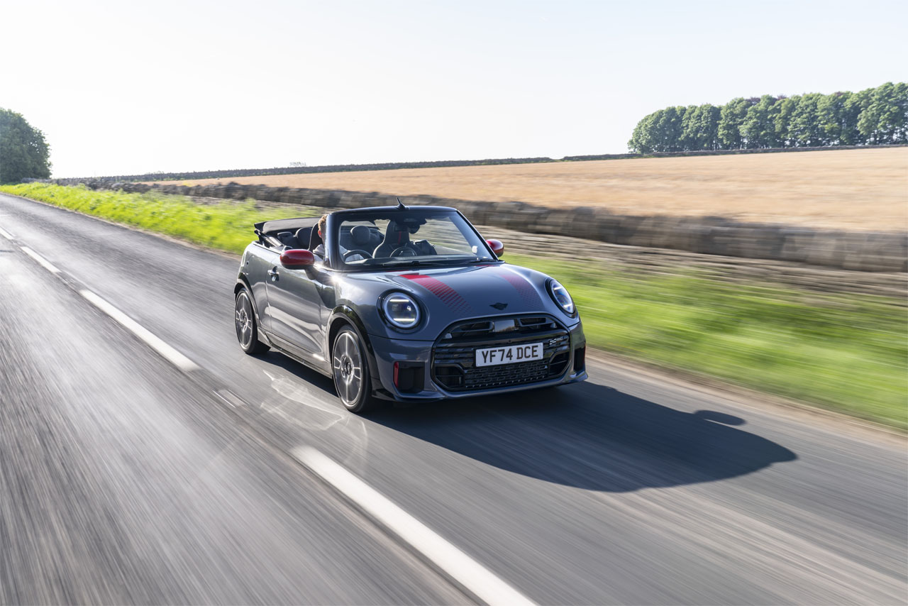  A Mini Cooper S Cabriolet in bright red, featuring a convertible roof, parked against an urban backdrop.