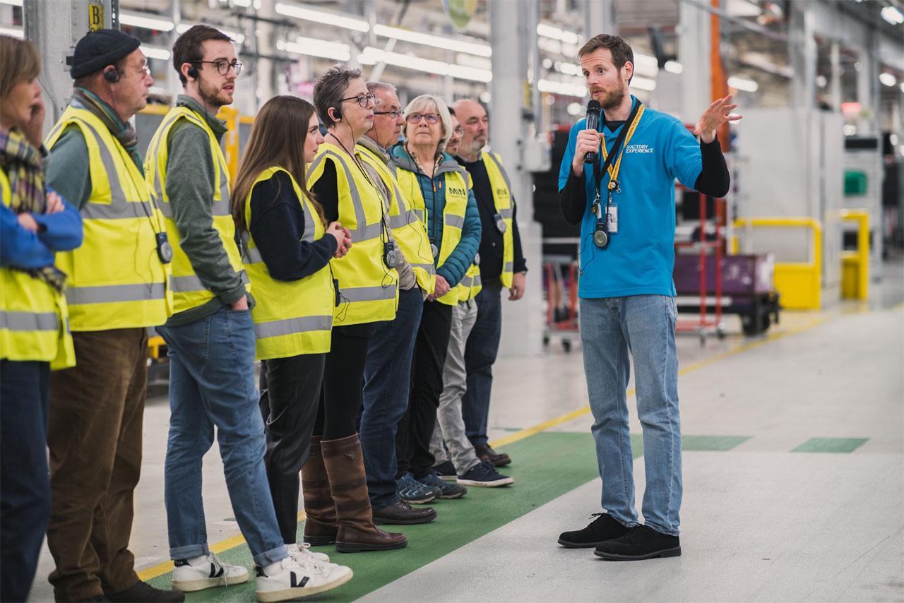 Several people gathered in a factory setting, engaged in conversation near large machines and production equipment.