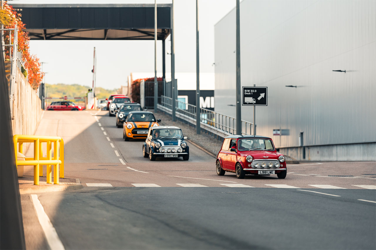 A convoy of vehicles moving along a road, flanked by grass and shrubs.