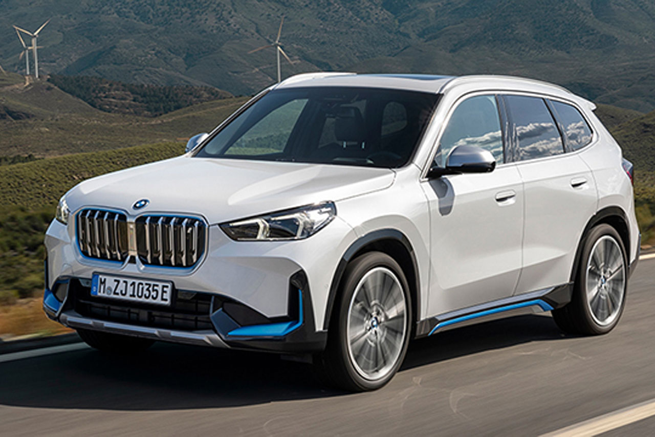 White BMW iX1 driving on a country road.