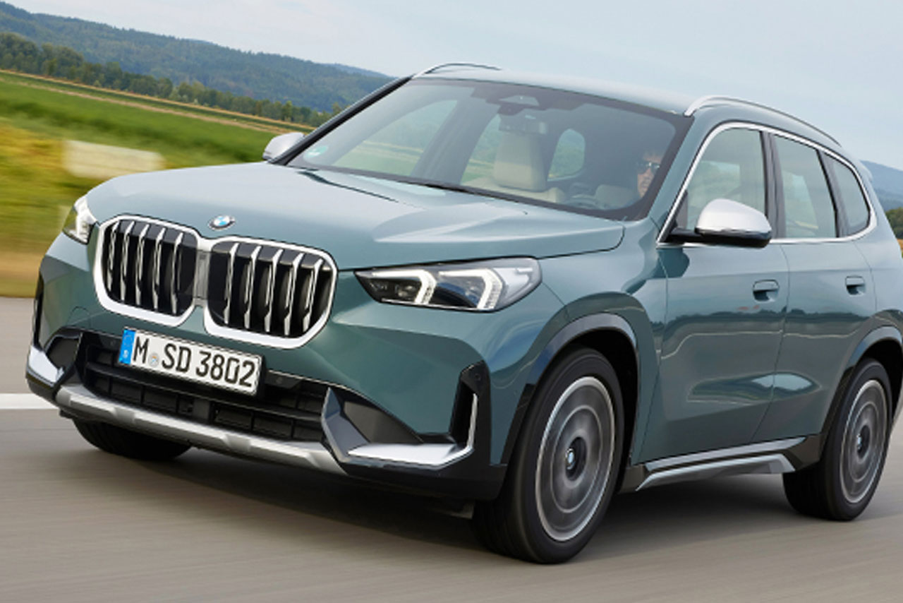 Gray BMW X1 on a road next to large fields.