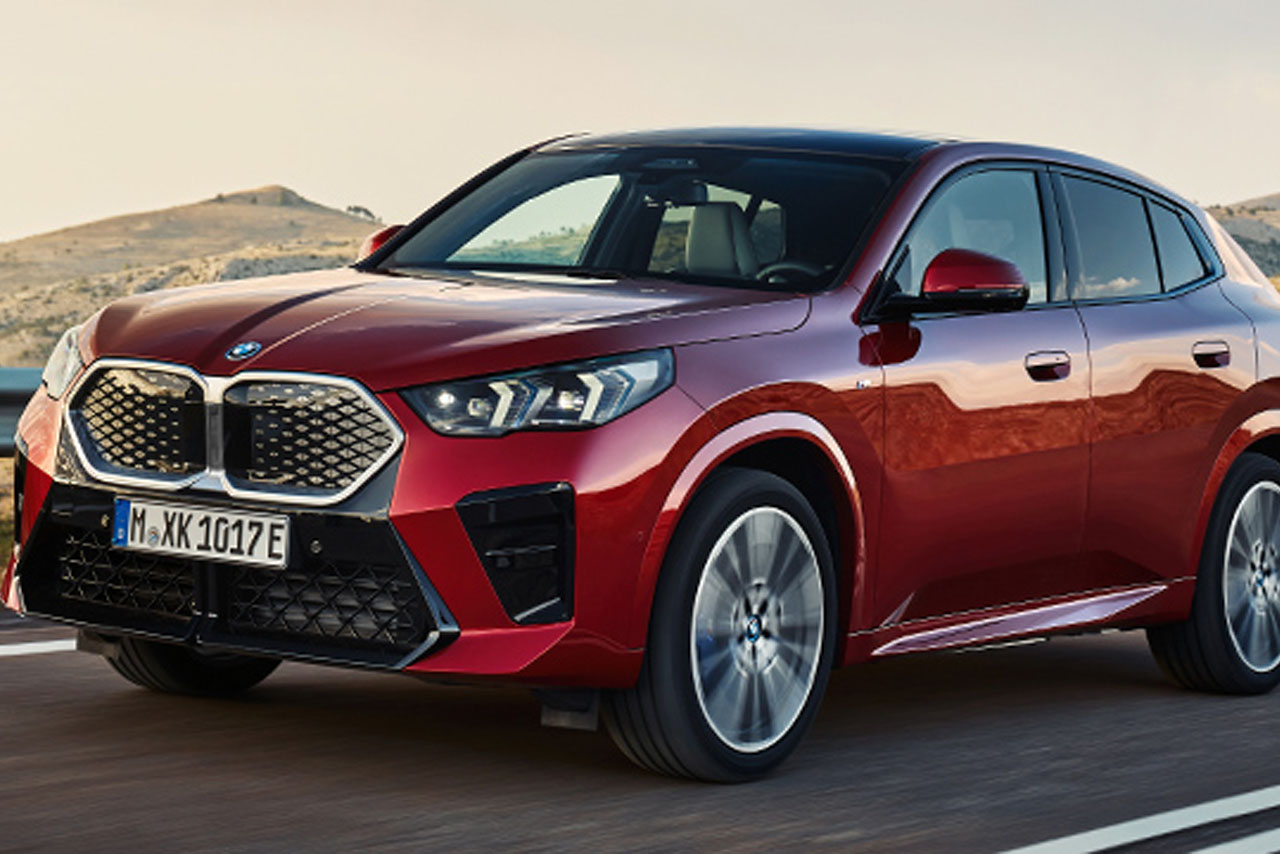 Red BMW iX2 drives along the sea.
