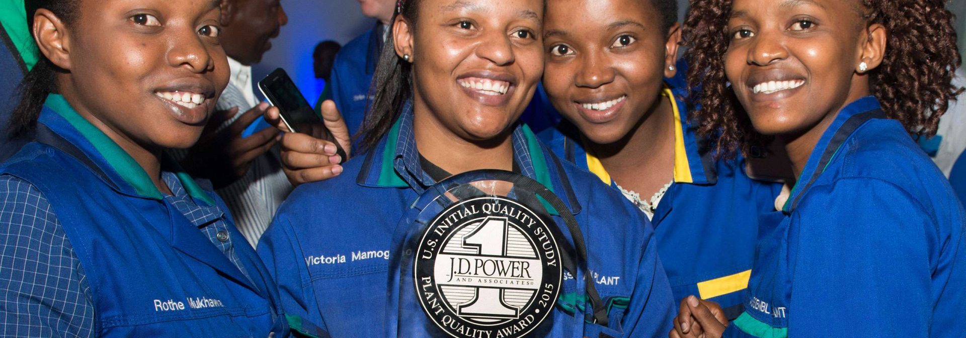 A group of four women in matching blue attire holds a plaque, showcasing their achievement with smiles.