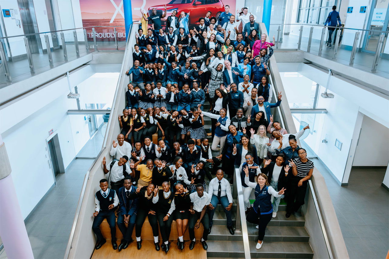 A diverse group of students stands on the stairs, smiling for a photo, capturing a moment of unity and joy.