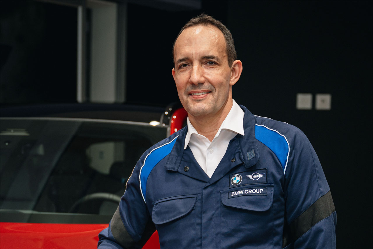 A man standing infront of a red BMW car smiling at the camera.