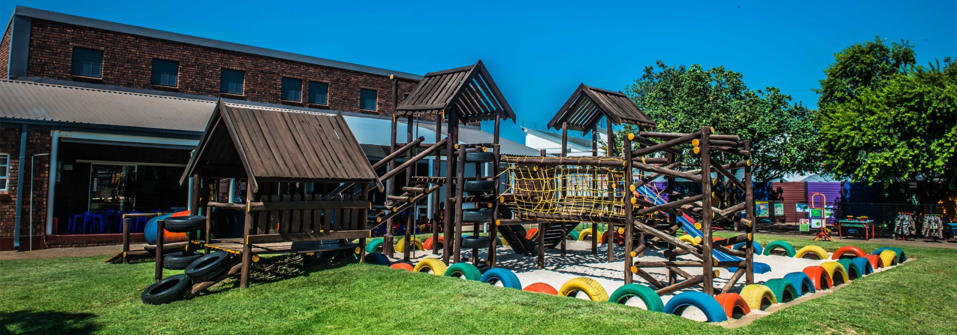 A playground featuring a wooden structure with a slide, surrounded by grass and trees, inviting children to play.