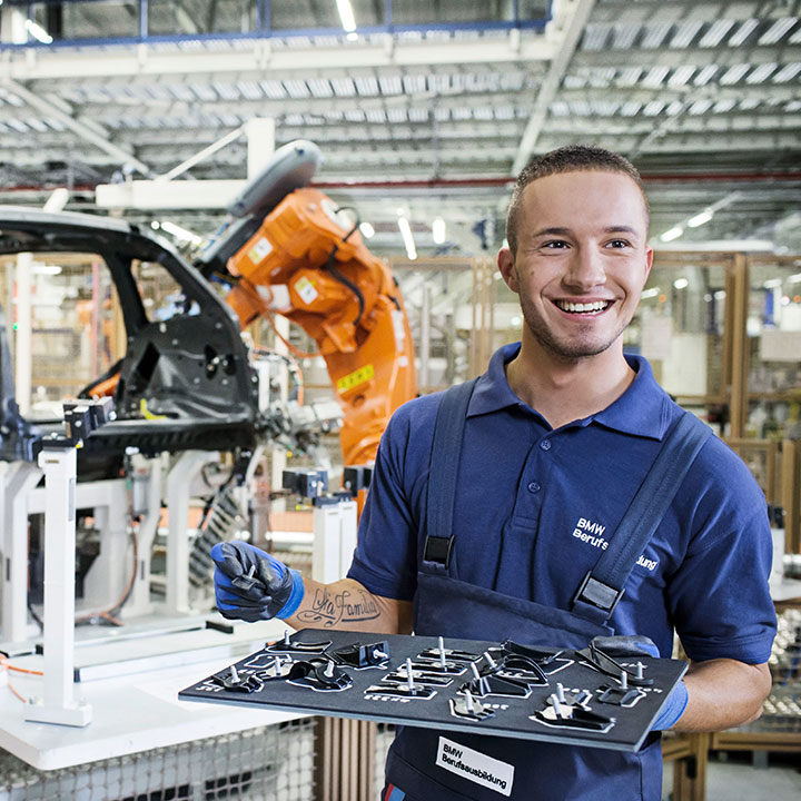 Apprentice working in the production at BMW Group San Luis Potosi with a robot in the background.