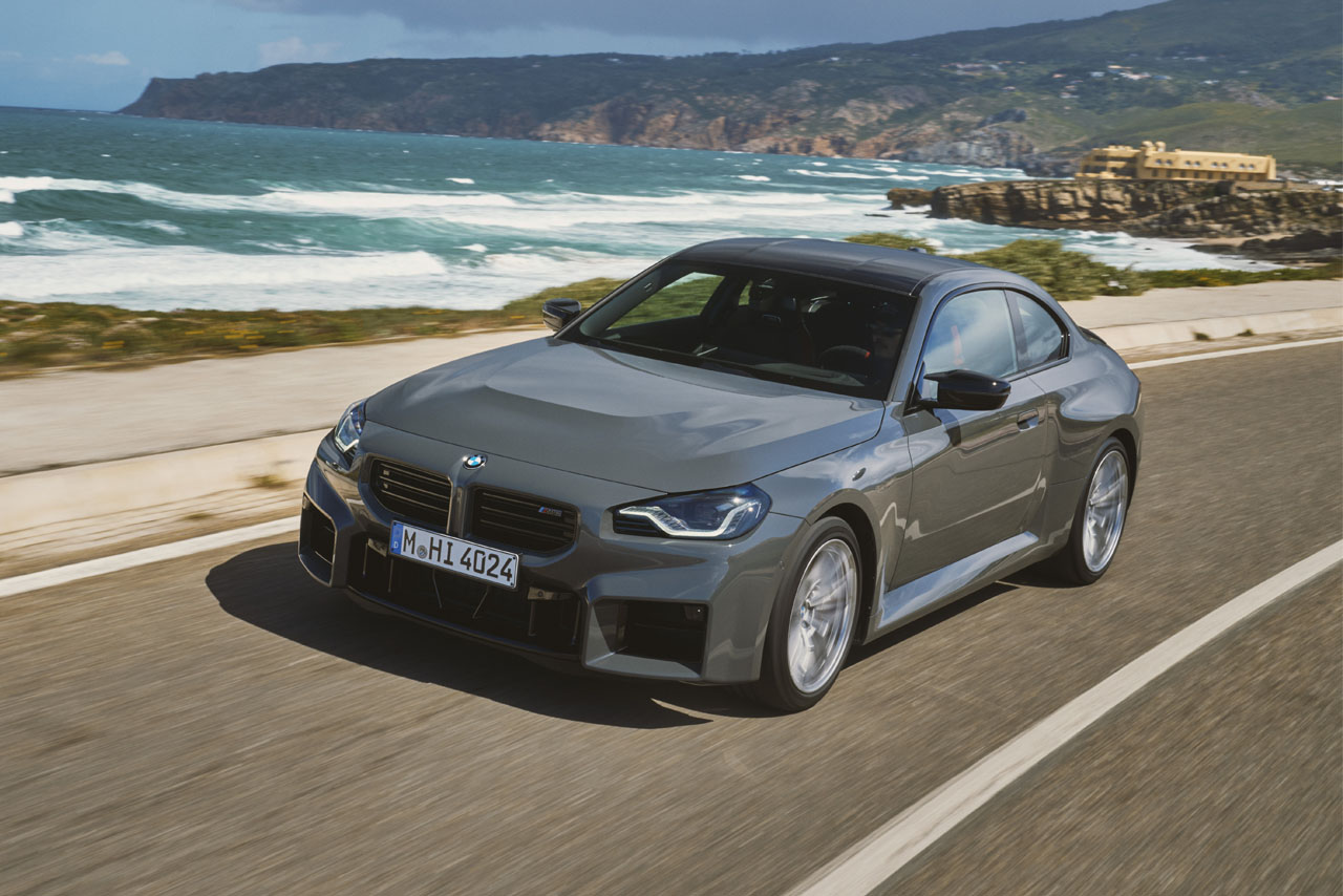 Grey BMW M2 driving on a road next to the sea.