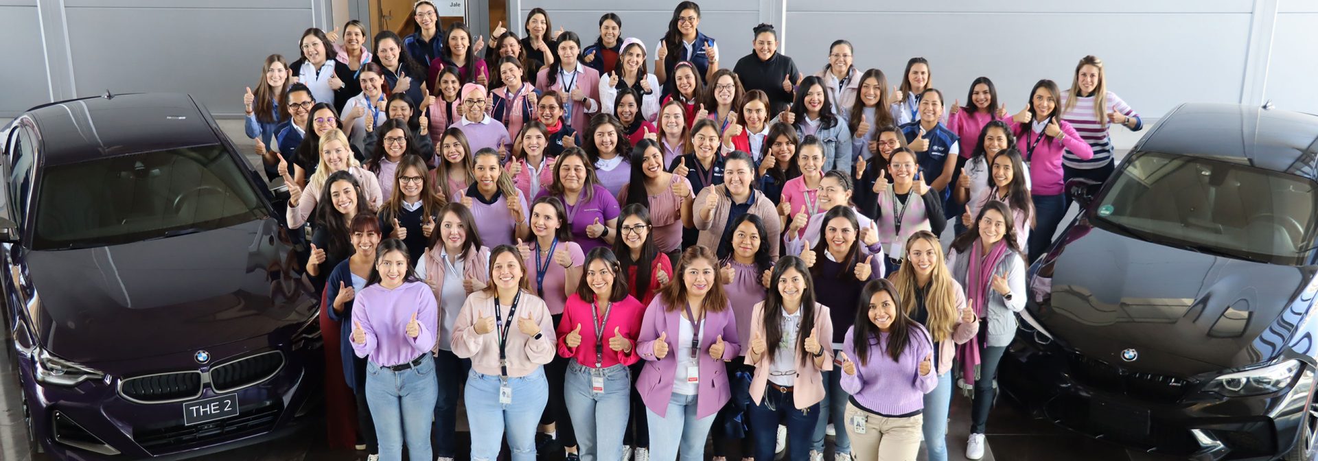 Female employees at Plant San Luis Potosi wearing pink tops posing with two BMW 2series for a picture.