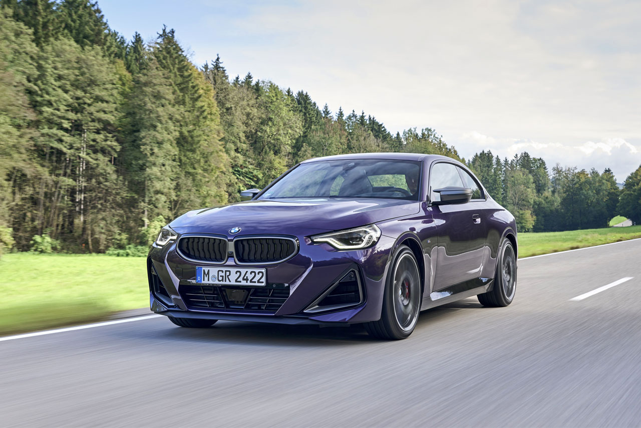 Purple BMW 2 series driving on a road through the woods.