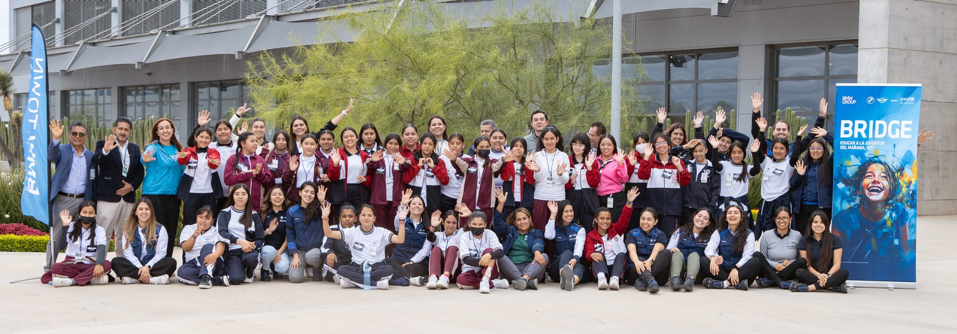 Gran grupo de personas sonriendo y saludando a la cámara.