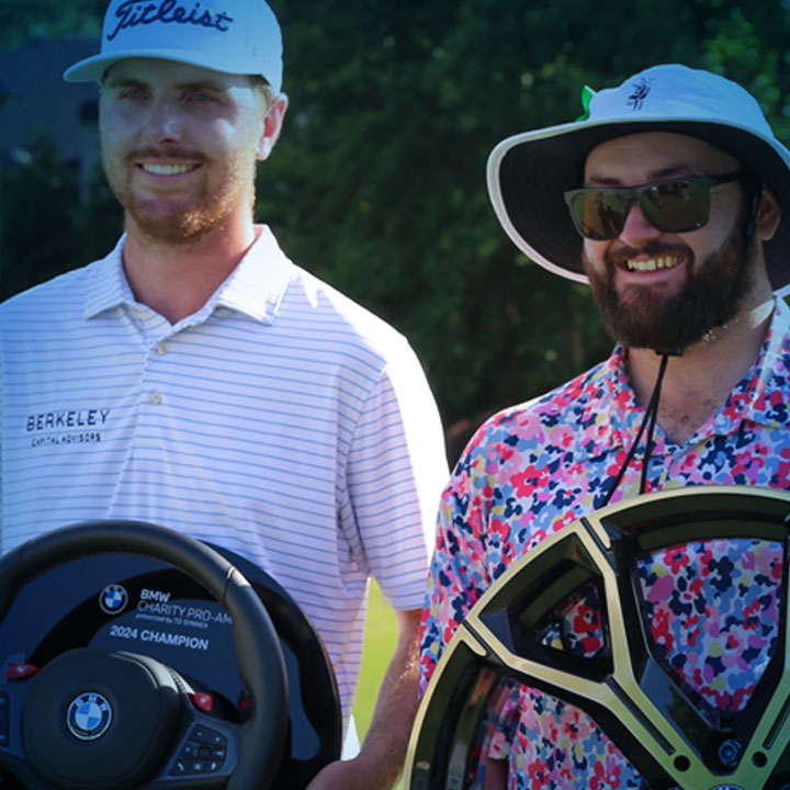 Two men in hats and shirts pose with their golfing trophies.
