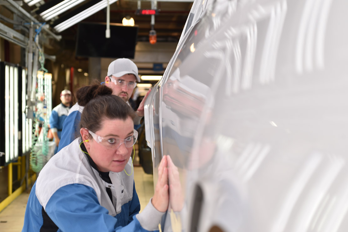 A woman in the Paint Shop checking the paint on a car.