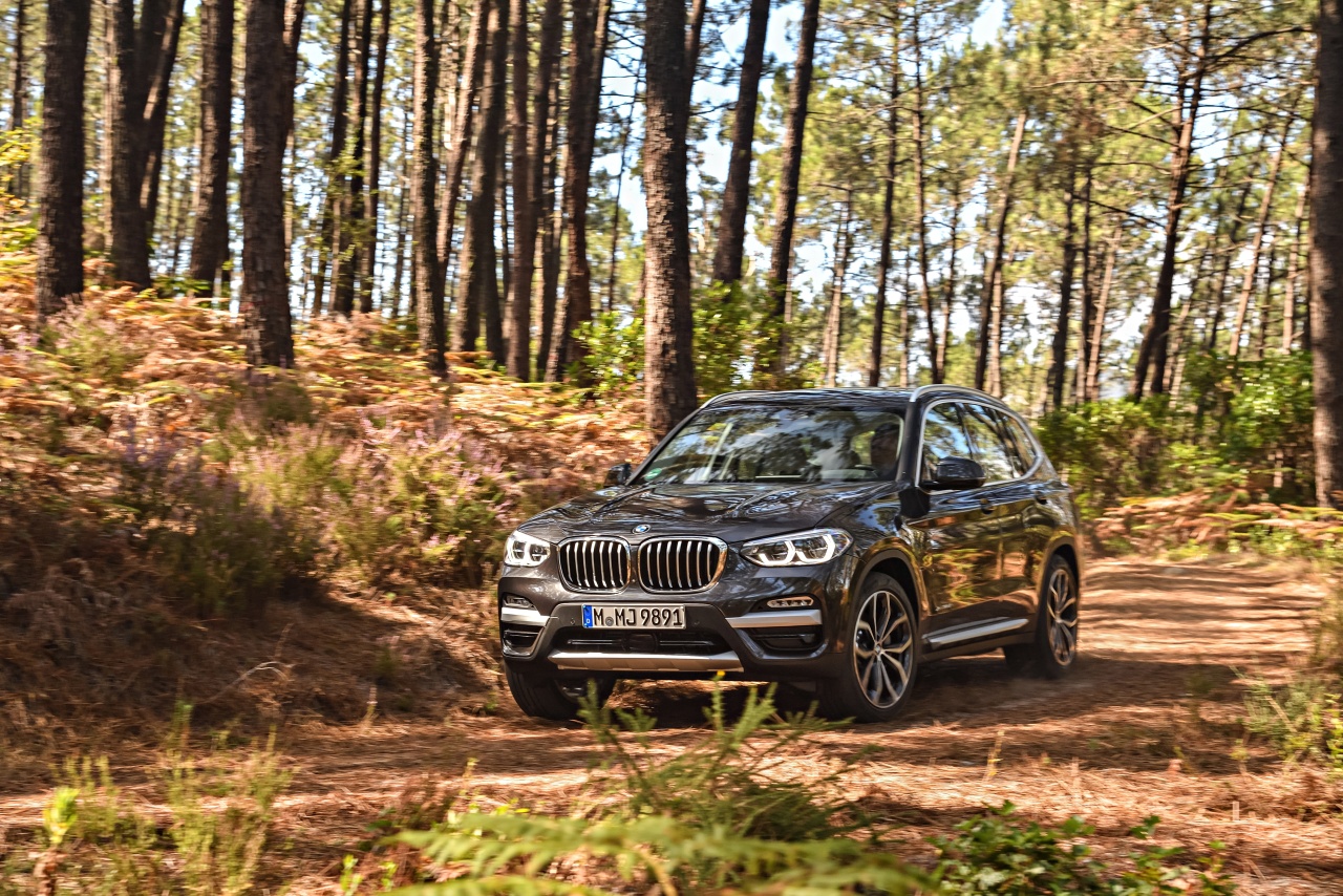 BMW X Model driving on a dirt road through the woods. 