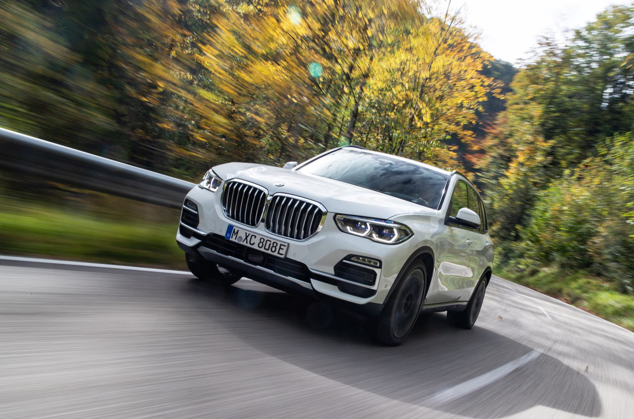 2021 BMW X5 xDrive45e PHEV driving on highway with beautiful green and yellow trees in the background. 