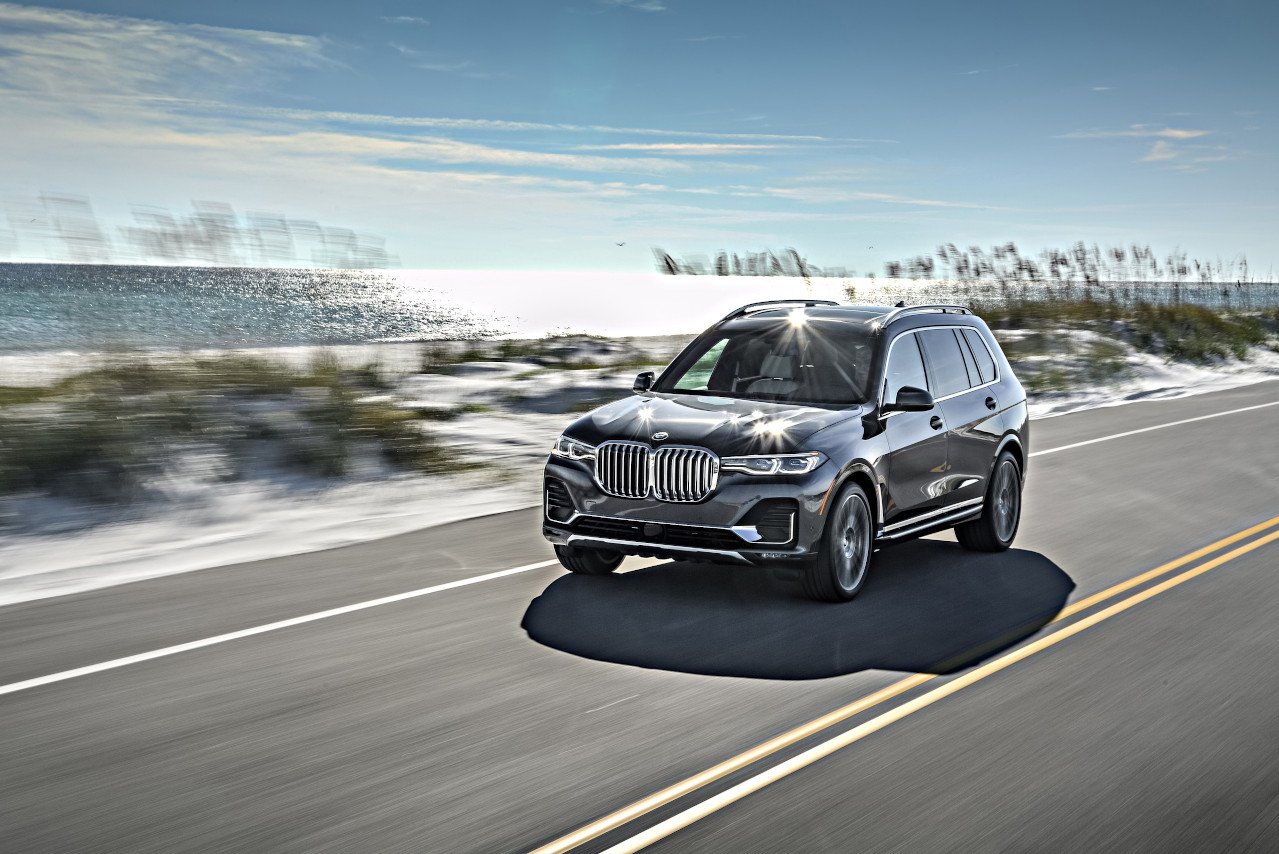 BMW X7 driving on a two lane road alongside the beach dunes. 
