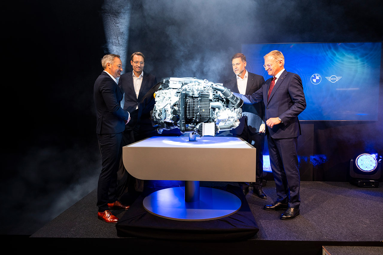 Vier Herren in Anzügen stehen neben einem Tisch, auf dem eine Maschine platziert ist.