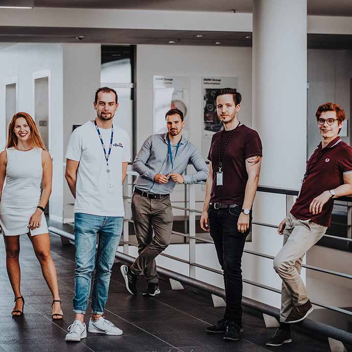 Fünf BMW Group Mitarbeiter posieren in einem Gang für die Kamera.